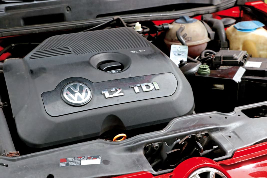 Zwischen Motorabdeckung und Batterie gut zu erkennen sind Druckspeicher und Hydraulikölbehälter des Gangstellers