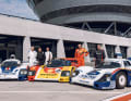 Die Gentleman-Driver kamen im August 2022 in Leizpzig zusammen. In ihrer aktiven Zeit gehörten sie zu den besten Rennfahrern der Welt. Von links: Derek Bell, Jochen Mass, Timo Bernhard, Hans-Joachim Stuck und Bernd Schneider. Hier sind sie an den Fahrzeugen zu sehen, mit dem sie einst die Rennstrecken dominierten. Links parkt der 956-002 Langheck (LH) im Rothmans-Outfit, in der Mitter der 962-009 Kurzheck (KH) im Shell-Design und rechzt der 956-005 Kurzheck in der Racing-Folierung (im Rothmans-Style).