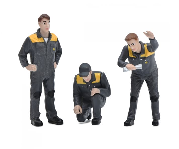 Die drei Figuren aus dem Set tragen einheitlich graue Arbeitsoveralls mit gelben Brustteilen und einem Kirovets-Logo. Ein Mechaniker kniet, ein weiterer hat zwei Werkszeuge in der rechten Hand.]Foto: Werk