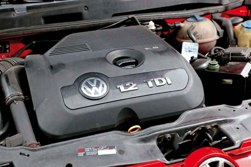 Zwischen Motorabdeckung und Batterie gut zu erkennen sind Druckspeicher und Hydraulikölbehälter des Gangstellers