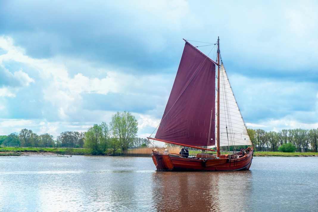 New construction of a historic pile ewer sails in the Elbe and mudflats