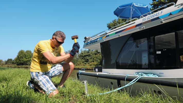 Blow by blow: the pegs are driven into the canal bank with a hammer to moor the boat