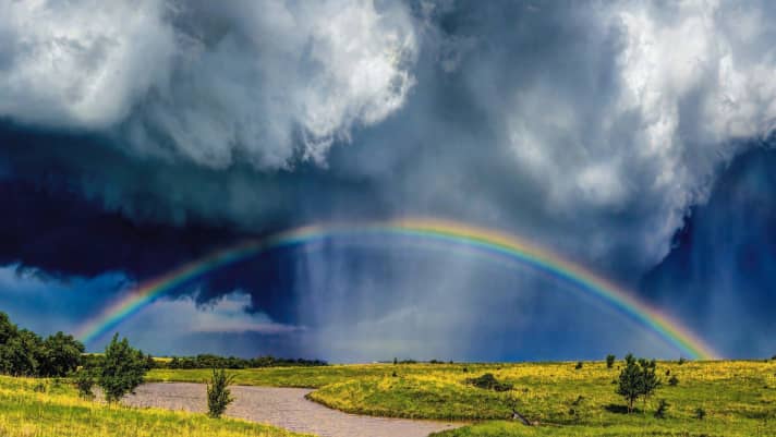 A storm has passed over the vastness of Oklahoma. Now the sun fights its way through the clouds and conjures up a rainbow on the rain curtain.