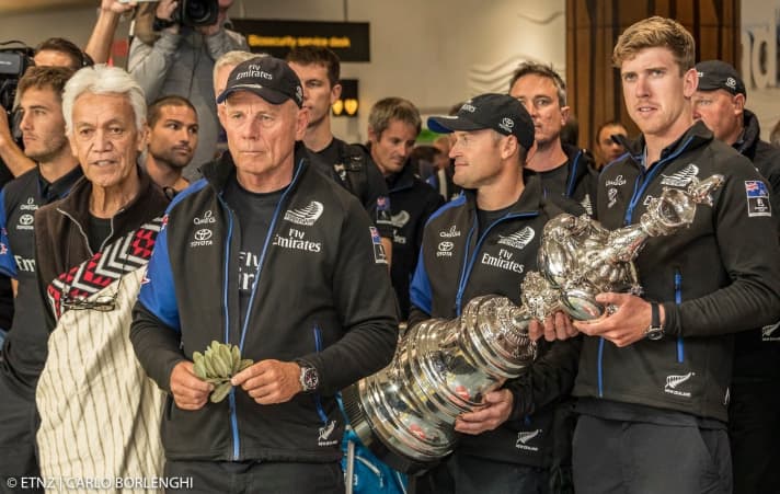   Ému, fier et certainement un peu fatigué : le barreur Peter Burling, le skipper Glenn Ashby et le chef d'équipe Grant Dalton (de gauche à droite) sont fêtés après l'atterrissage à Auckland.