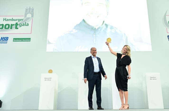   Di buon umore sul palco di gala: la direttrice del Team Malizia Holly Cova regge il premio per lo Sportivo dell'Anno di Amburgo come se Boris Herrmann, arrivato dalla Francia, potesse raggiungerlo. Anche il lodatore Prof. Dr. Mojib Latif si rallegra del premio per la lotta contro il clima.