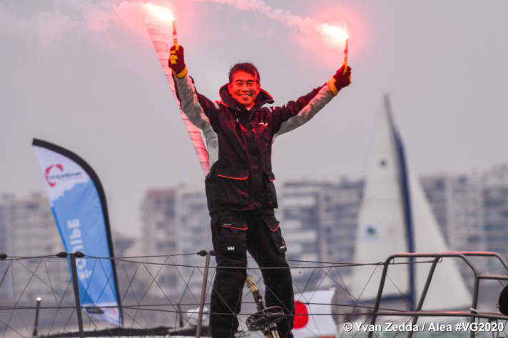   Kojiro Shiraishi con il tradizionale bengala in entrambe le mani sul ponte di prua del suo "DMG Mori Global One" mentre entra nel porto di partenza e arrivo di Les Sables-d'Olonne