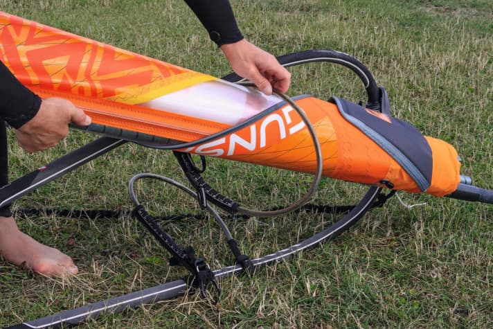 Your boom should act as a handle. It usually works better if you push the boom together beforehand. Push the sail pulley and mast through a harness rope...