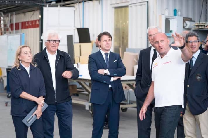   Italy's Prime Minister Giuseppe Conti visited the Luna Rossa Prada Pirelli team on the occasion of the christening of the new "Luna Rossa" in Cagliari. Skipper Max Sirena explains the boat, team president Patrizio Bertelli and his wife Miuccia Prada can be seen on the left of the picture