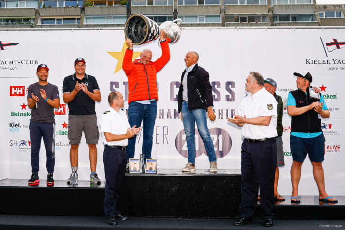   Qui, il campione del mondo di Starboat Frithjof Kleen solleva il piatto più grande della 127a Kieler Woche nel cielo di Kiel. Insieme al suo timoniere italiano Diego Negri, il berlinese, che vive sul lago di Garda, è stato felicissimo di salire sul gradino più alto del podio del 99° Campionato del Mondo Starboat.