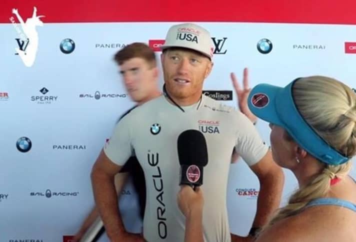   Für Humor zu haben: Peter Burling formt seine Finger im Rücken von Jimmy Spithill schon einmal zum V für Victory. Jetzt haben sich die Kiwis im Video zur Vorstellung der neuen Cup-Boote wieder einen Scherz mit Spithill erlaubt und seine Stimme eingebaut