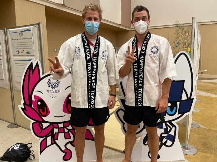   Erik Heil et Thomas Plößel devant les mascottes olympiques japonaises Miraitowa (à droite, Jeux olympiques) et Someity (Jeux paralympiques). Les mascottes ont été choisies par les écoliers japonais. Mirai" signifie "futur", "towa" "éternité". Les personnages se voient attribuer des super-pouvoirs. Ainsi, Miraiowa doit pouvoir se téléporter d'un endroit à l'autre - un rêve également pour les navigateurs olympiques.