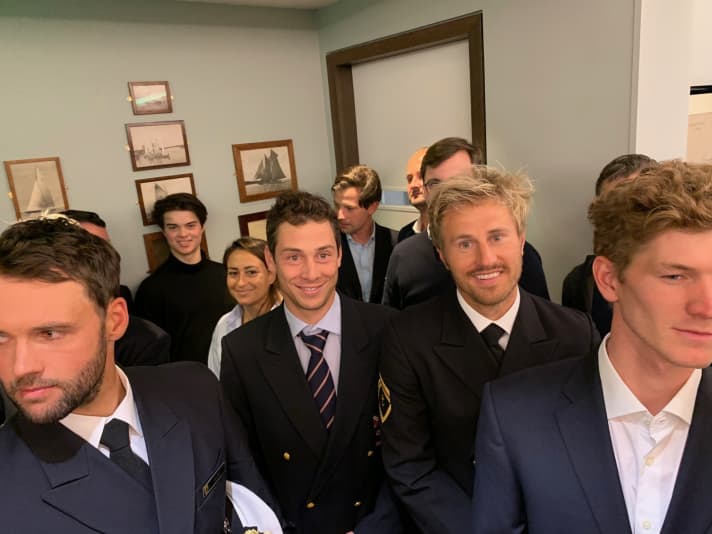   Juste avant la cérémonie d'hommage : les médaillés de la German Sailing Team et leurs coéquipiers du NRV. Parmi eux, le sparring partner de Buhl, Nik Aaron Willim, Erik Heil, Thomas Plößel et Philipp Buhl (de droite à gauche). Plus loin sur la photo : Lena Erdil, nouvel espoir du surf au sein de l'équipe olympique NRV, et le fils de Thomas Frisie et barreur Nacra-17 Silas Mühle, qui a fait la promotion de la participation d'une équipe hambourgeoise axée sur la performance à la Youth America's Cup.