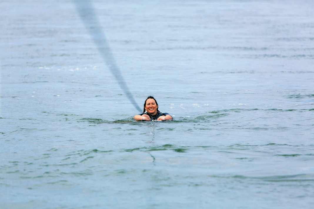 Schritt 1: Position im Wasser einnehmen – Rückenlage mit Blick zum Boot. Board steht quer zur Zugrichtung. Knie sind stark angewinkelt, Füße  zeigen nach oben. Arme gestreckt, außerhalb der Knie. Leine gerade nach vorne halten.