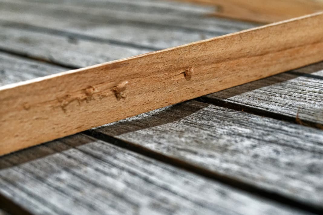 Die Latte macht deutlich, wie unterschiedlich das Holz verwittert und vom jahrzehntelangen Schrubben aus­gewaschen ist. In diesen Tälern würde das Epoxidharz Seen bilden, daher müssen sie eingeebnet werden
