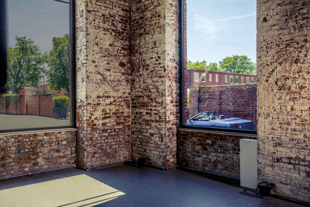 Sehnsucht im Blick.   In der alten Industrie-architektur ist der offene Sportwagen im Fensterrahmen ein Symbol für die Freiheit des Fahrens und für das Ende der Ziegelzeit.