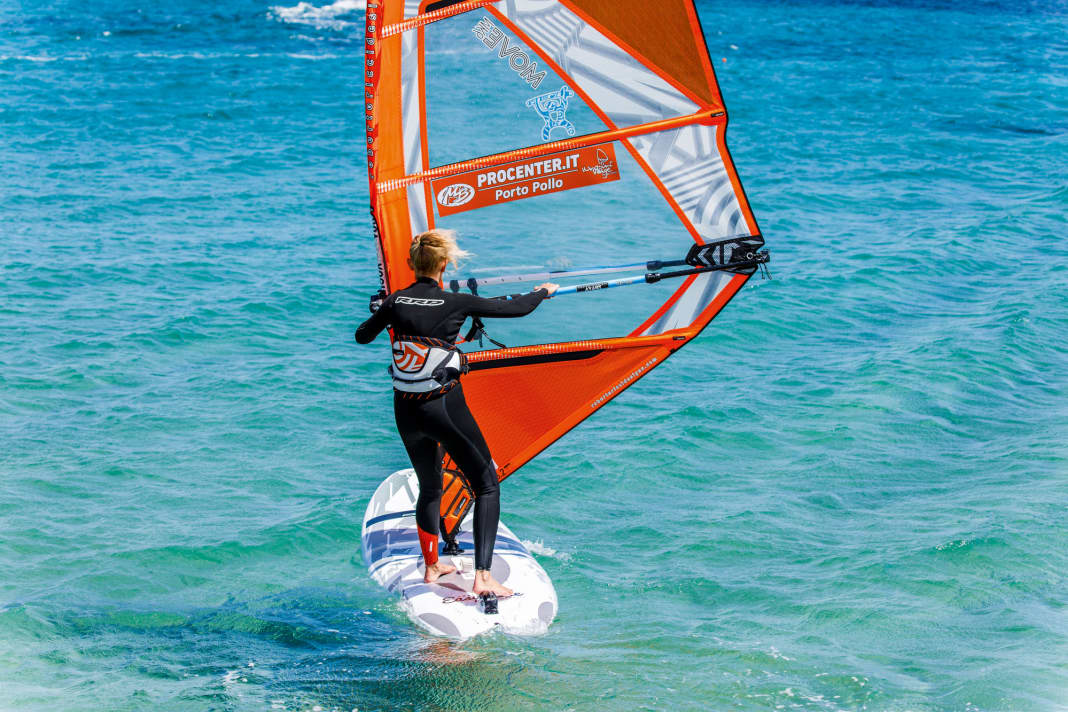 Die Halse beim Windsurfen Schritt für Schritt: Hole wie immer nach dem Start erstmal etwas Schwung und bereite die Halse vor, indem du die Segelhand am Gabelbaum etwas nach hinten in Richtung Gabelbaumende verschiebst.