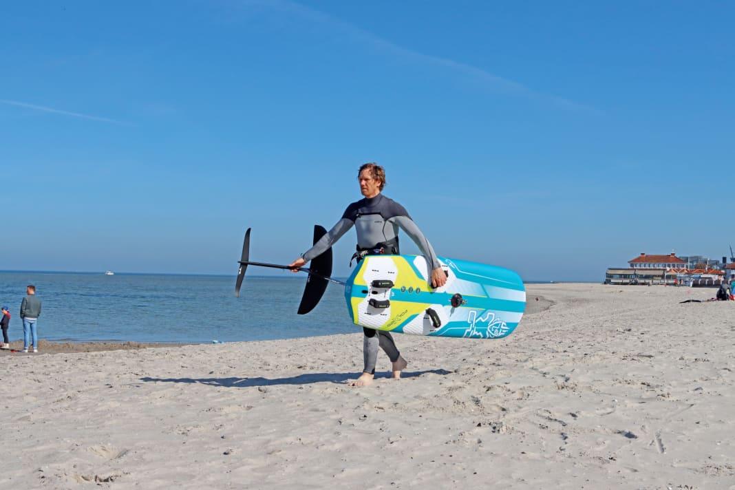 Wie immer gilt: Zuerst das Brett, da dir dieses am Strand nicht so schnell wegfliegen kann. Greife mit einer Hand die vordere Schlaufe des Boards, die andere Hand greift an der Fuselage. Der Vorteil dieser Technik ist, dass du das Foil beim Laufen immer sehen kannst.
