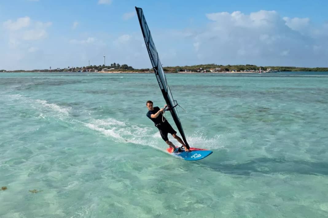 1) The foot change for the duck tack takes place before you duck. To ensure this is successful, ease off the sail slightly and, on a light broad reach, switch your feet by first moving your front foot back (heel-to-heel) and then immediately moving your back foot forward towards the mast foot. You can initiate the duck tack from a half-planing or full-planing position on a half-wind course. After a successful foot change, luff slightly again.