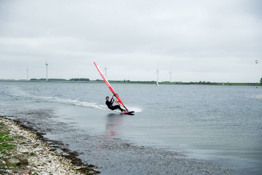Place your back foot in front of the foot strap, unhook yourself from the harness at full planing speed and start on a light upwind to half-wind course (with your arms already bent) by gently placing only your front leg on the surface of the water first. Hold the sail close to your body, especially with your front hand. You can repeat this several times as a preliminary exercise to familiarise yourself with the feeling.