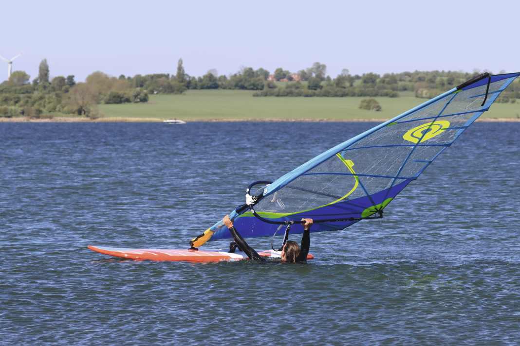 First, place your front hand on the mast, then your back hand on the lower leech.