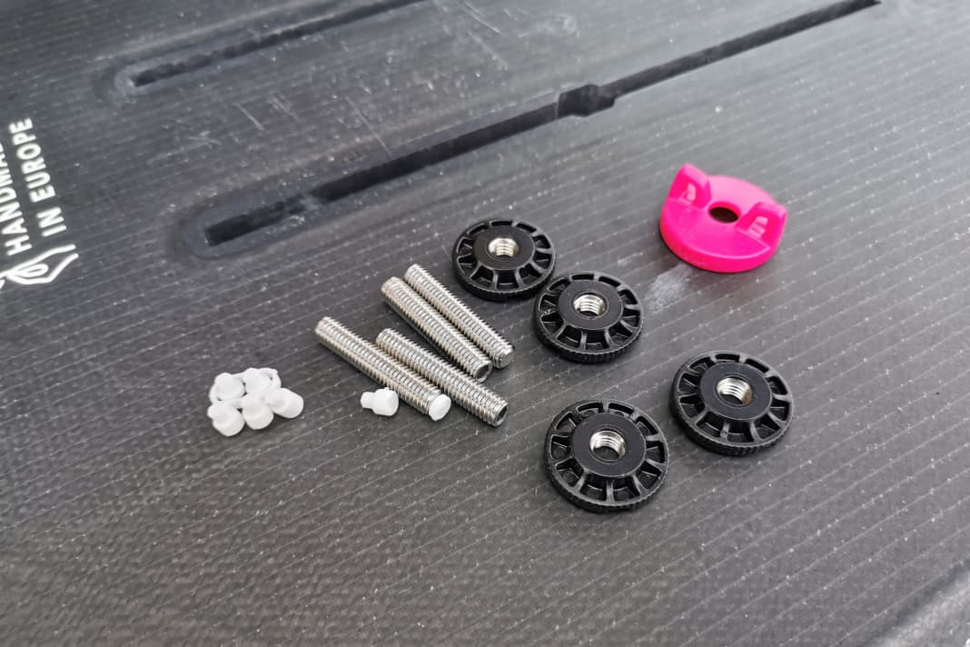 Das FoilFix Set besteht aus Stehbolzen, kleinen Spacern (weiß) zum Anpassen der Schraubenlänge, den Muttern (schwarz) und einem kleinen Werkzeug (pink)