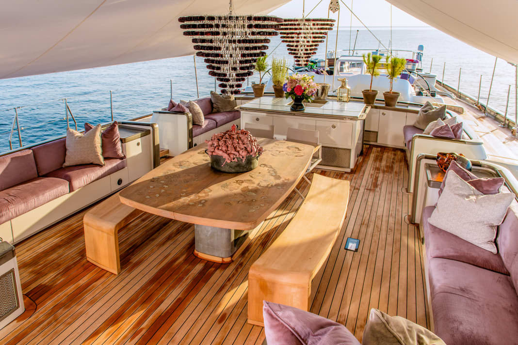 Sous le taud de soleil : à l'avant, le grand cockpit pour les invités avec table à manger, deux candélabres de Murano sont suspendus à la grande bôme. Il est directement relié à l'office en dessous.  La sculpture en bronze au milieu de la table est l'œuvre de l'artiste cubain Roberto Fabelo.