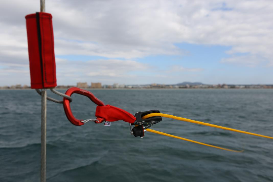 1 : Ouvrir la valise, sortir le mousqueton marqué 1 et l'accrocher à un want ou à l'amarrage de la bôme.