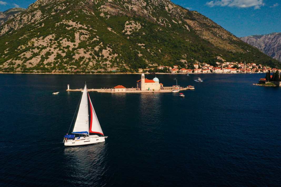 Yacht de location devant Gospa od Skrpjela, en français : Marie du Rocher. En arrière-plan, la ville portuaire de Perast
