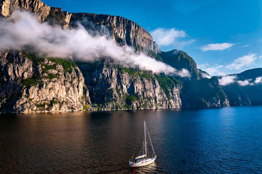 A narrow band of cloud runs along the flank of a rocky wall on the Lysefjord. In front of it is the author's yacht. It gives an idea of the enormous dimensions of the rocks