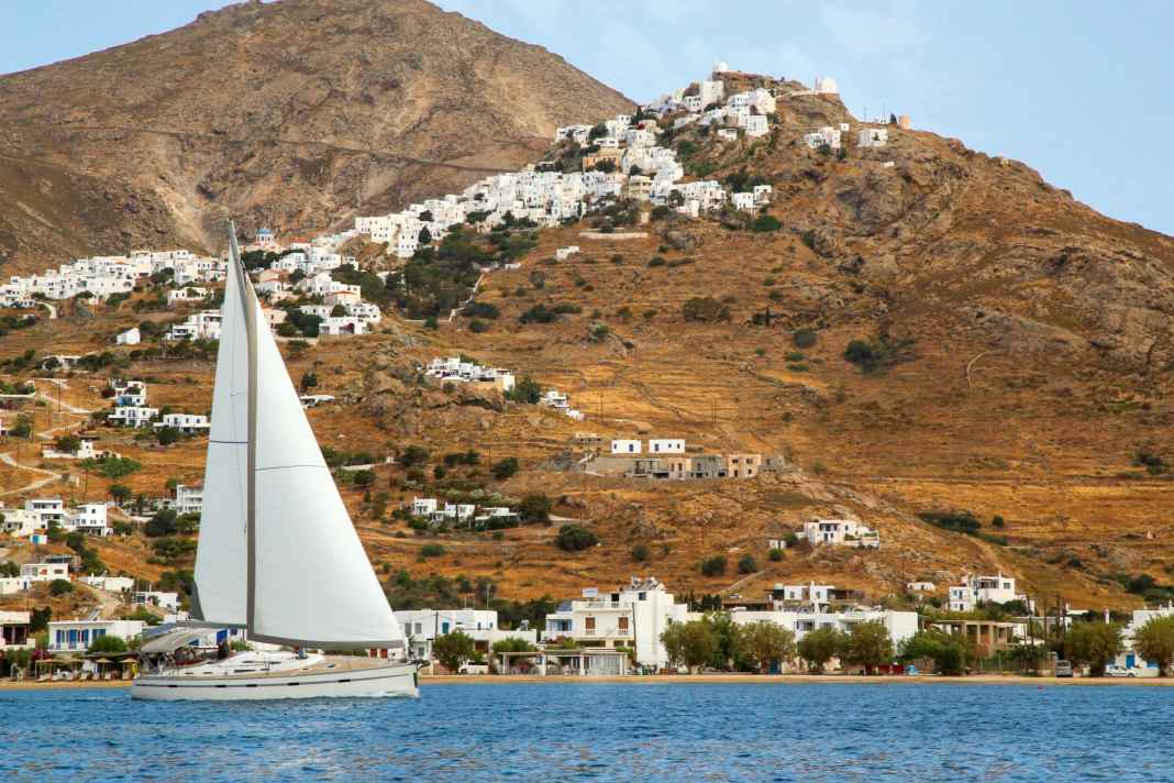 Eine Yacht segelt in der Bucht Livadi am Fuß der Altstadt von Serifos. Die thront hoch oben am Berg und ist unbedingt einen Besuch wert