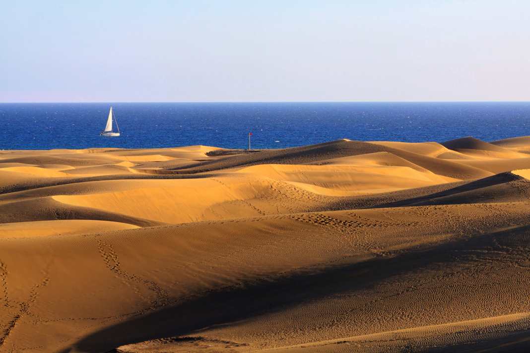 Una barca a vela gira intorno alla punta meridionale di Gran Canaria, le suggestive dune di Maspalomas. Il Sahara è vicino.