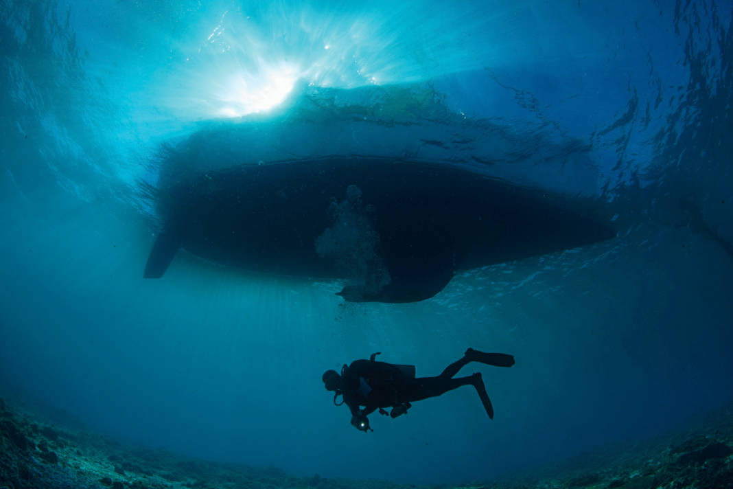 Mystérieux et magique à la fois : un plongeur en scaphandre autonome flotte lentement sous un voilier.