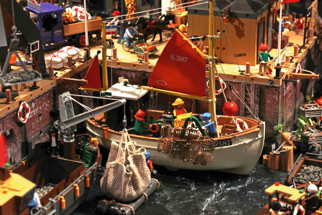 Umschlag im Miniatur-Hafen: Ein kleiner Ladekran hievt Frachtgüter von einem historischen Holzschiff an die Kaikante.