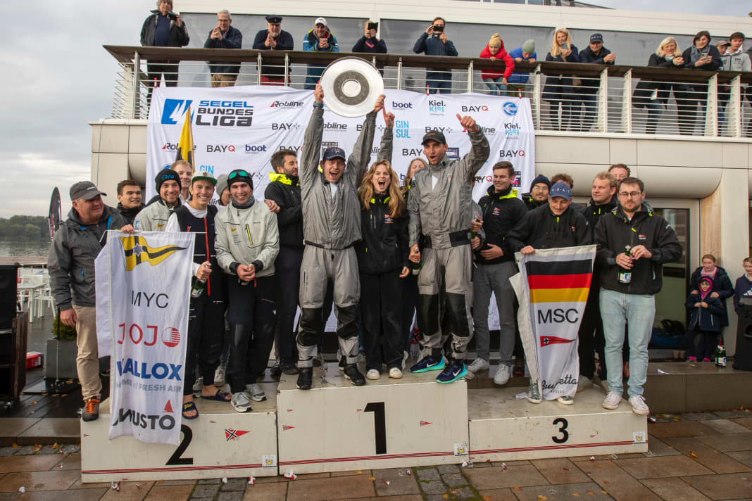 Die Rekordmeister vom NRV jubeln über Titel Nummer sieben seit 2013, Steuermann Tobias Schadewaldt streckt die Meisterschale in den Himmel. Flankiert werden die Sieger von den Vizemeistern vom Münchner Yacht-Club und den Saison-Dritten vom Mühlenberger Segel-Club