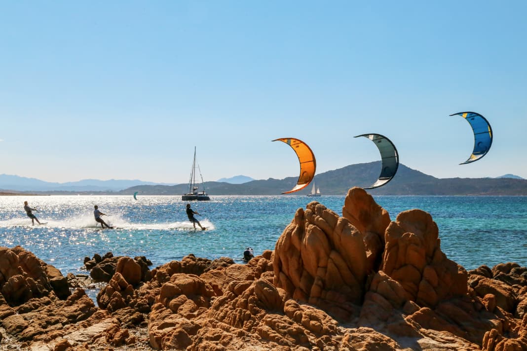 Sören, Jan and Philipp fly in formation across the bay in the evening light. The cat's professional skipper has kitesurfing experience himself and selects the next spot depending on the wind forecast and the crew's preferences. He keeps an eye on the kiting guests and can come to the rescue with the rib if necessary