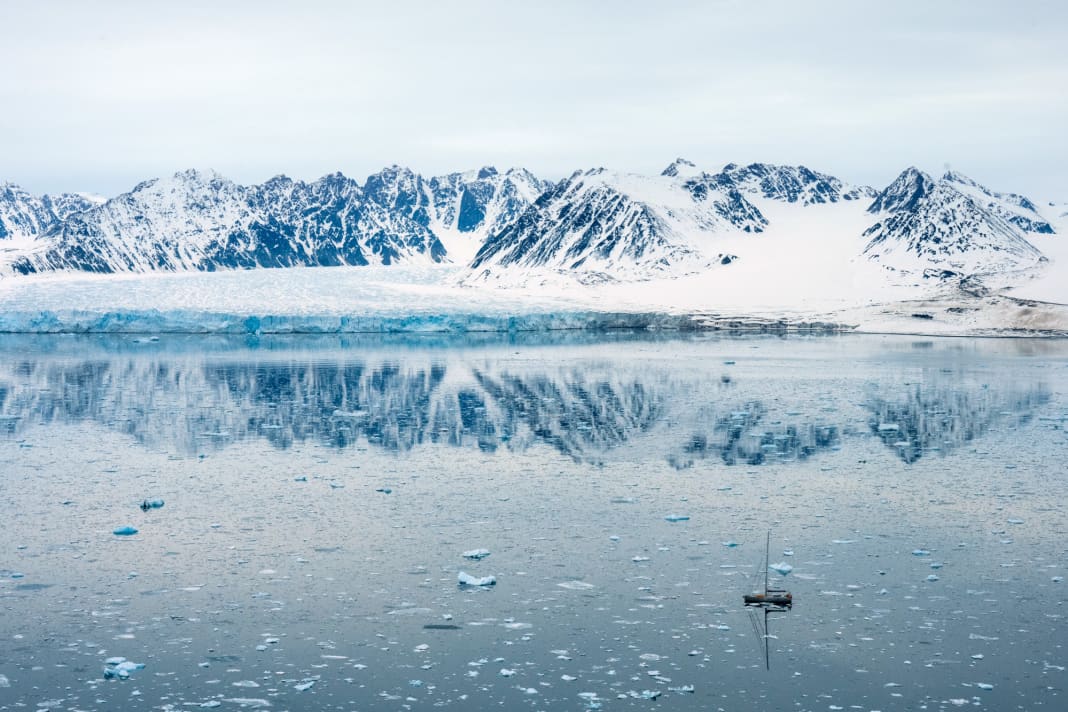 Die 66-Fuß-Aluyacht „Qilak“ im Eisfeld vor den schneebedeckten  Ber­gen und einem der Gletscher an der Westküste Spitzbergens