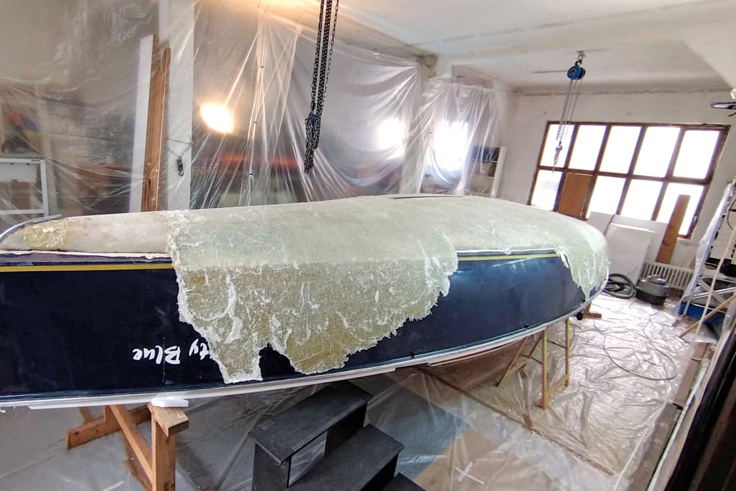 In a fortunately available workshop, Maximilian Kolb strips the laminate layers, which are barely separating from each other, from the hull with a spatula