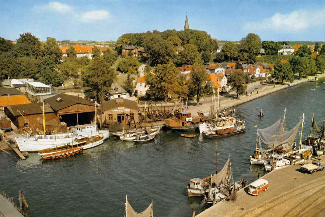 Neben dem roten VW-Bus liegt der Kutter des Großvaters von Martin Hüdepohl, der mit dem Wiki “Eckekutter” die Geschichte der Fischerei in Eckernförde dokumentieren und bewahren möchte. Der große weiße Kutter ist ein Neubau der Eckernförder Siegfried-Werft. Davon wurden sechs Stück gebaut und nach Island verkauft.