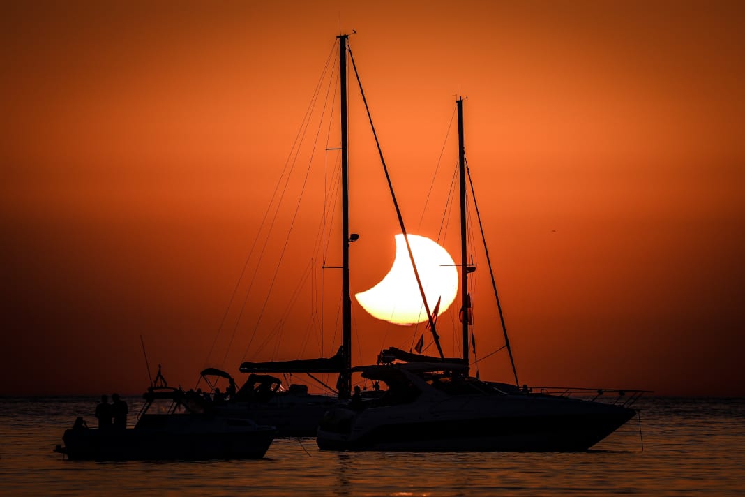 L'eclissi solare prosegue dietro gli alberi delle barche a vela.