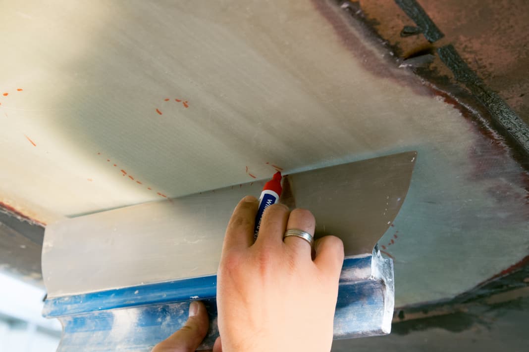 After curing, the peel ply is removed. The levelling of the laminate can then begin. Firstly, mark the raised areas that protrude beyond the hull strake. A large palette knife or a batten is suitable for this purpose