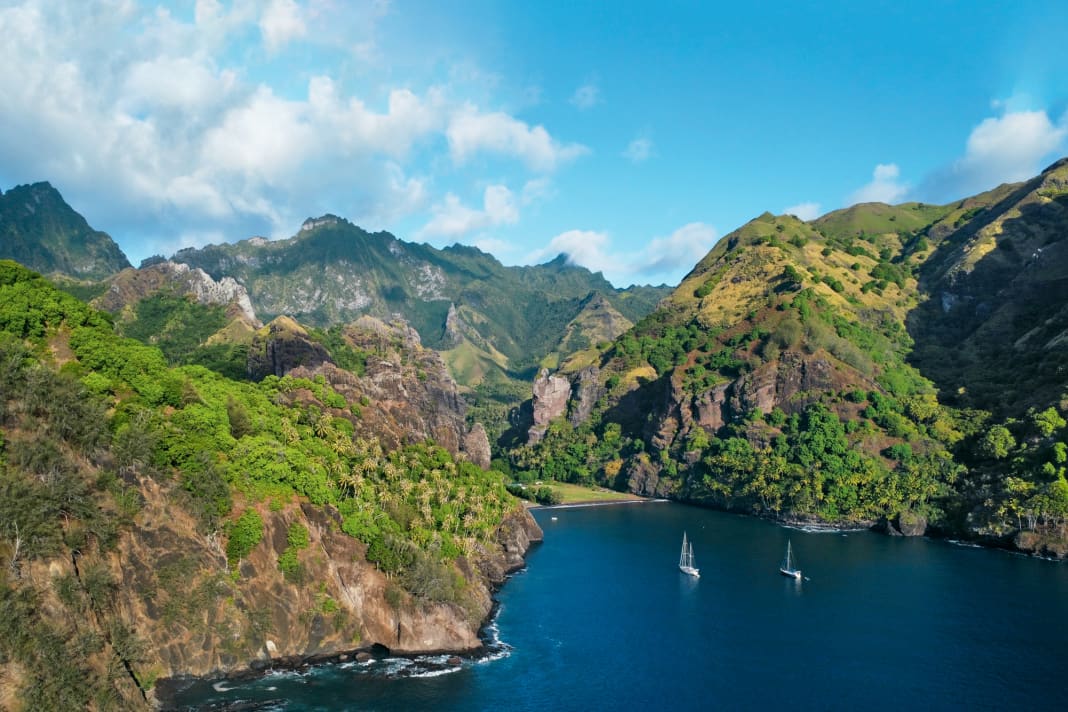 Deux voiliers d'eau bleue au mouillage dans la baie des vierges sur la côte ouest de Fatu Hiva.  Dans l'étroite vallée entre les rochers se trouve le village de Hanavave