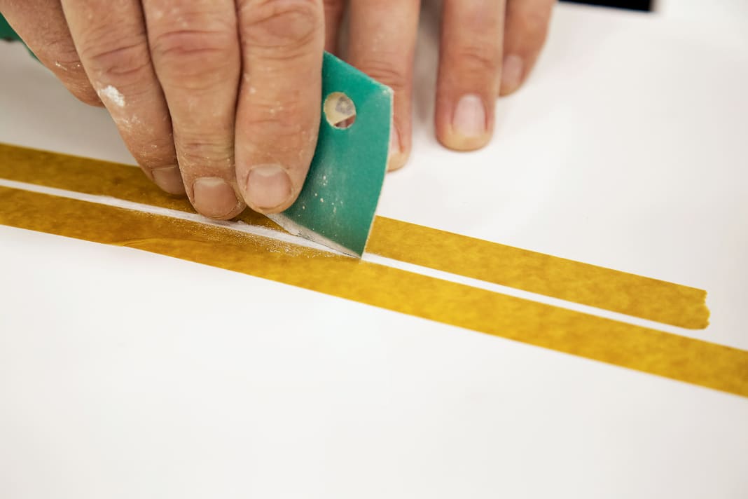 Die Kanten der Schramme mit 120er-Papier schräg schleifen. Das Klebeband schützt die Umgebung vor Kratzern
