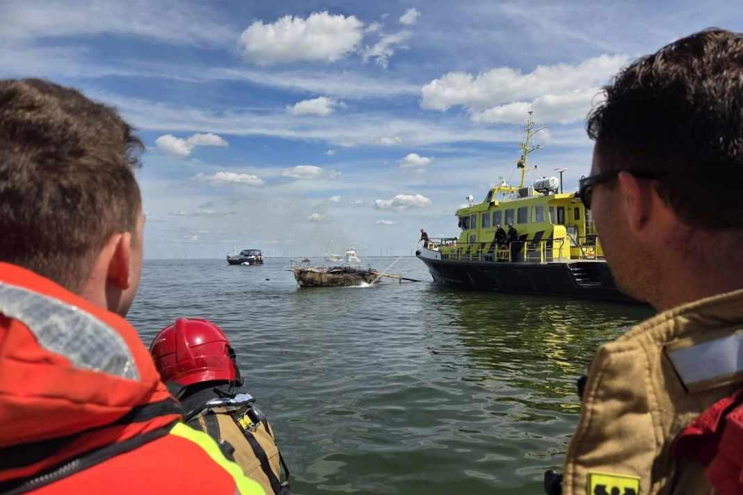 Ein Besatzungsmitglied der KNRM-Station Urk und ein Feuerwehrmann der Station Urk schauen zu, wie das Segelboot gelöscht wird.
