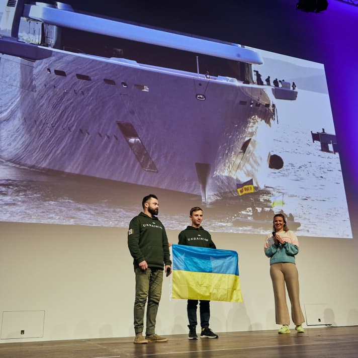 Die Seamaster-Ehrung mit Laudatorin Anastasiya Winkel aus dem Olympiakader des German Sailing Team, Opti-Steuermann Sviatoslav Madonich und Pavlo Dontsov. Im Hintergrund zeigt ein Ausschnitt aus dem bewegenden Film, den Nils Günter für die Seamaster-Ehrung produziert hat, die Protestaktion der Opti-Gruppe gegen die Abramovich-Megayacht “Solaris”