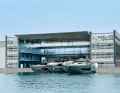 Zentrale: Hinter nachtblauer Fassade und unter einem  Dach in Flügelform liegen Büros. Im fast identischen Gebäude gegenüber werden Yachten abgeliefert oder konfiguriert.  Sogar die Poller leuchten in Riva-Aquamarin