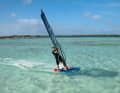 2-3) The aim is to move the sail exactly in the direction of the relative wind, only then will it hover neutrally. The relative wind results from the airstream and the wind actually blowing - it therefore does not blow directly from upwind, but diagonally from the front. To duck, release the front hand from the boom and, as with a duck jibe, reach crosswise backwards onto the end of the boom. Push the mast forwards at an angle towards the water. By applying slight pressure to the windward edge, your board will continue the turn to windward.
