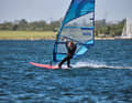 1st preparation phase: Before you think about taking the step into the loops, you first need to get up to the necessary speed. To do this successfully, you should set your board up on a light space wind course, i.e. the course diagonally away from the wind. The space wind course is the fastest course in surfing and therefore the chance of making it over the glide threshold is highest here. Hook into the harness, turn your upper body forwards - as described on the previous page - and make sure that your front foot is turned in the direction of travel on the deck. By turning the body forwards (front foot, chest), the power transfer to the board is directed forwards. If, on the other hand, the front foot is on the board at right angles to the direction of travel, the upper body automatically turns with it - this results in lateral forces that push the tail away to leeward and turn the bow into the wind. During this preparation phase, try to make contact with the loop with the front heel. This will allow you to place your foot in the loop without eye contact during the next step.