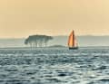 A sailing boat sets course for the Schlei in the reddish shimmering light of the evening sun.