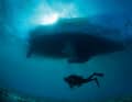 Mystérieux et magique à la fois : un plongeur en scaphandre autonome flotte lentement sous un voilier.