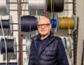 Metzger in his shop, standing in front of a shelf of rope on a reel.